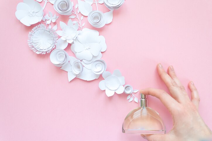 Women's hand spray perfume. Flower arrangement. Flowers, fragrance, perfume on pink background. Cut from paper