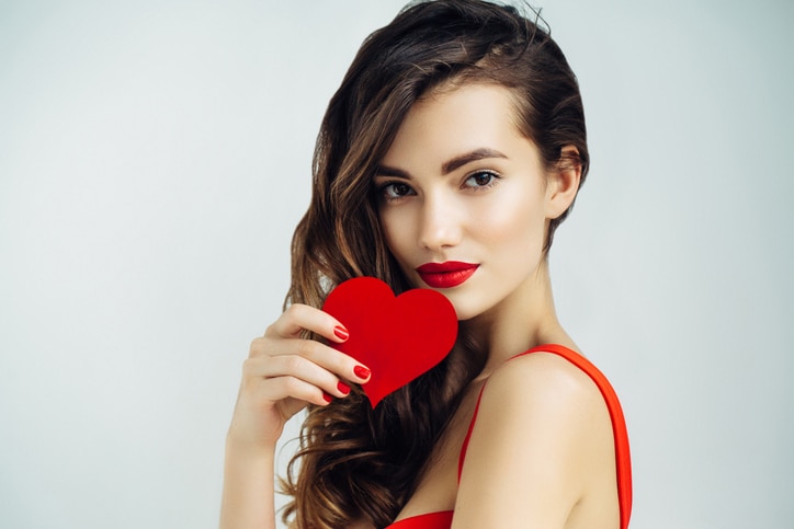 Studio shot of young beautiful woman holding artificial heart. Professional make-up.