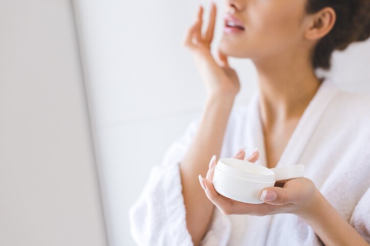 cropped shot of beautiful woman in bathrobe applying face cream