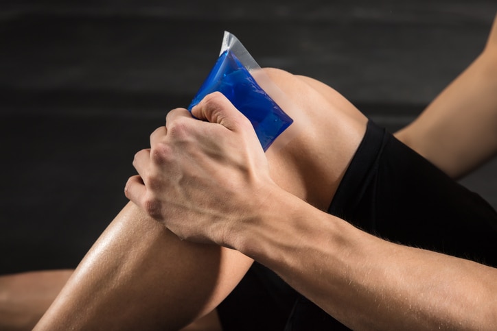 Close-up Of A Person Applying Ice bag On An Injured Knee In The Gym