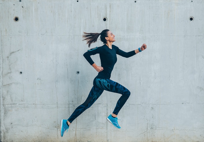 Woman passing by a wall while jogging in the city.