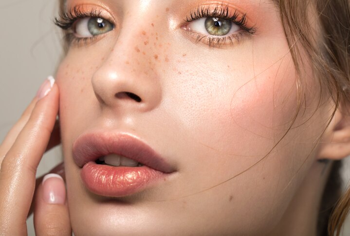 Closeup studio shot of a beautiful young woman with freckles skin posing against a grey background