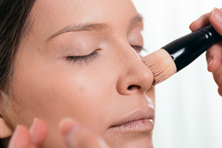 Make up artist applying liquid face powder foundation to a female client's face with a make up brush