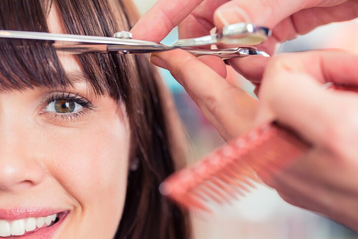 Hairdresser cutting woman bangs hair in shop