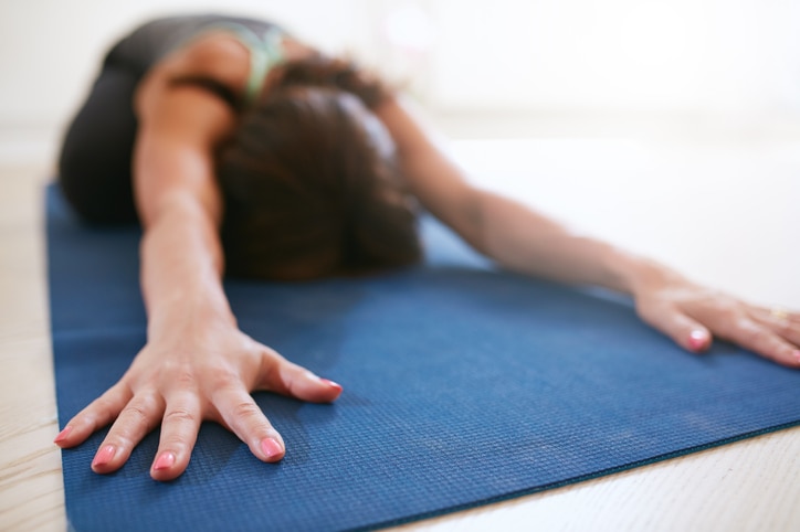 Woman stretching forward, performing a yoga pose on exercise mat. Fitness female performing balasana yoga at gym, focus on hands.