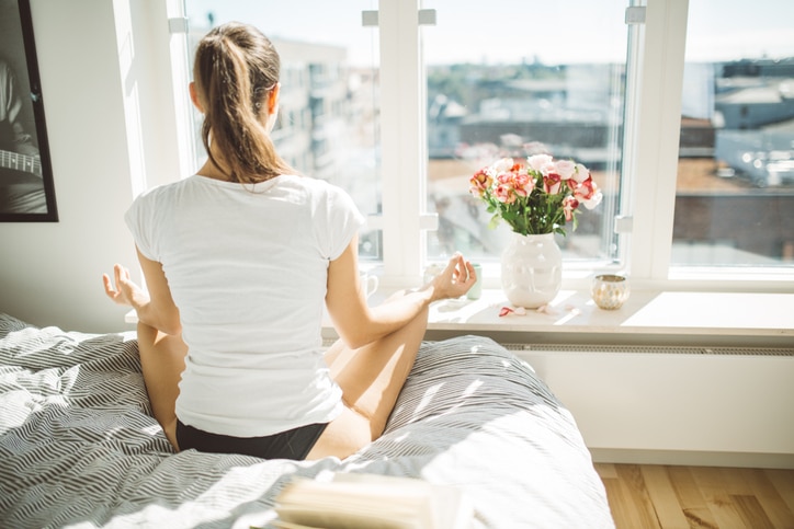 Beautiful woman practicing yoga in front of window of cozy apartment.Relaxation and mindfulness concept.Performing yoga in lotus position.