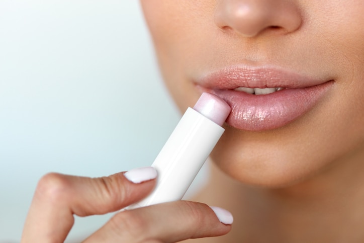 Lips Skin Care. Beautiful Woman Face With Full Lips Applying Hygienic Lip Balm, Lipcare Stick. Closeup Of Female Face With Soft Skin Putting Lip Protector Lipstick On. Beauty Cosmetics Concept