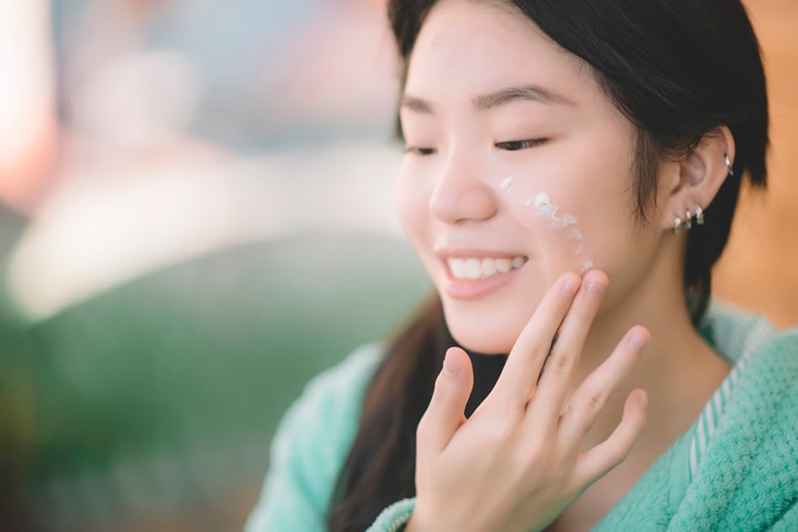 an asian chinese teenager girl applying moisturiser facial cream on hand and face