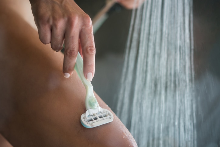 Close up of unrecognizable woman shaving leg with razor during morning shower in the bathroom.