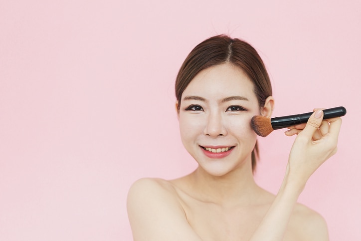 Beautiful Attractive Asian women smile with make up brush touching on her face perfect skin with copy space feeling so happiness and confident,isolated on pink background