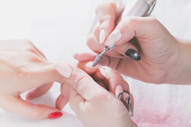 The hands of the master of manicure and the hands of the client close-up during the nail design process.Preparation for varnishing using special electric tools. Bright light, tinted.