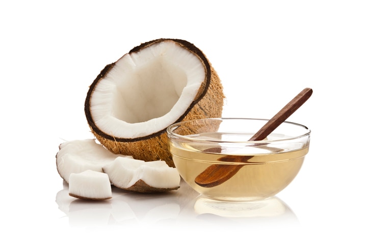 Glass bowl filled with coconut oil and half coconut with pieces isolated on white background