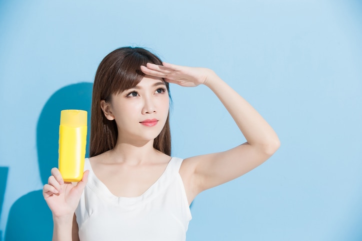 woman take sunscreen and look somewhere on blue background