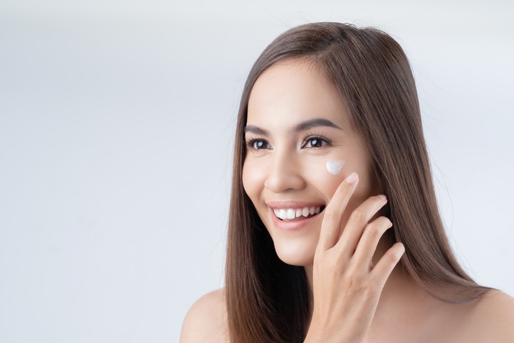 Asian woman. She is applying lotion on the face.