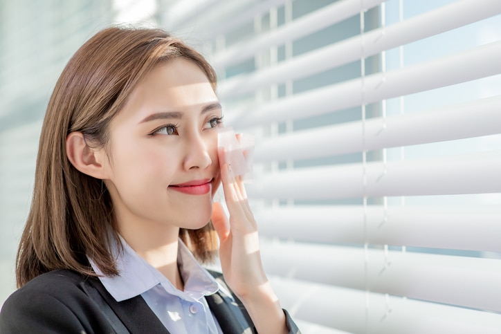 Young asian businesswoman smile and use oil blotting paper on her face