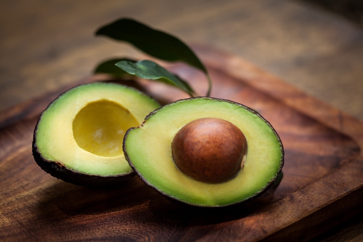 Avocado Halves on a wooden board with avocado leaves