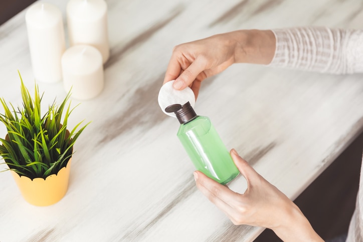 Makeup remove skin care. Closeup woman holding cotton swab and makeup remover liquid cosmetic in hands. Woman cleaning her face with lotion and cotton pad. Woman holding bottle with skin care product.