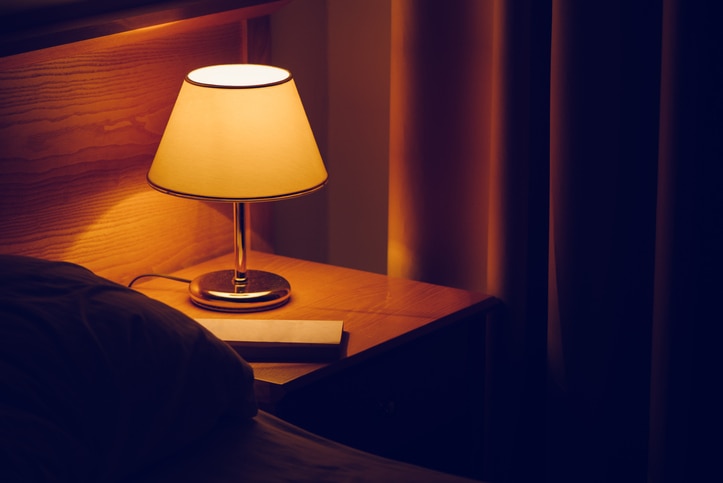 Electric lamp and book on bedside table in bedroom, selective focus