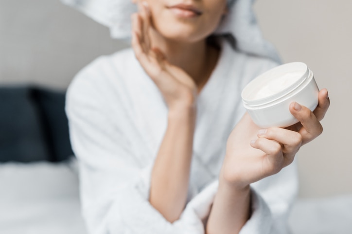 cropped view of girl applying cosmetic cream on face