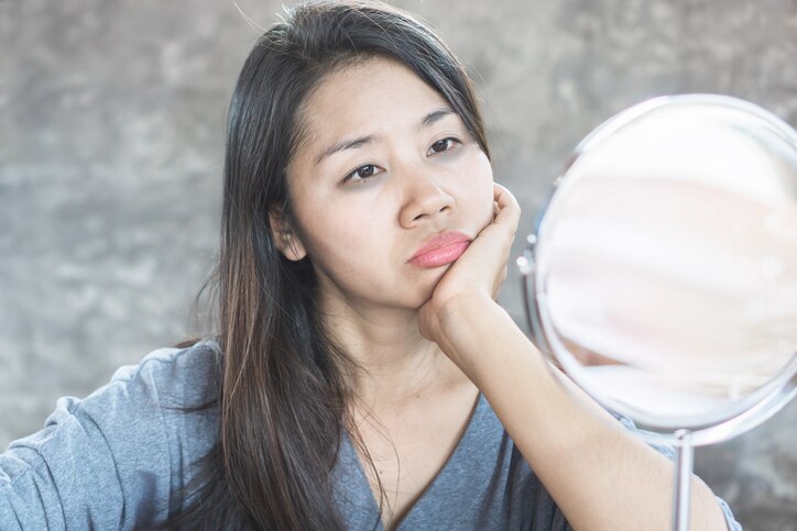 unhappy Asian woman age 40 checking her dark eyes circle problem in mirror