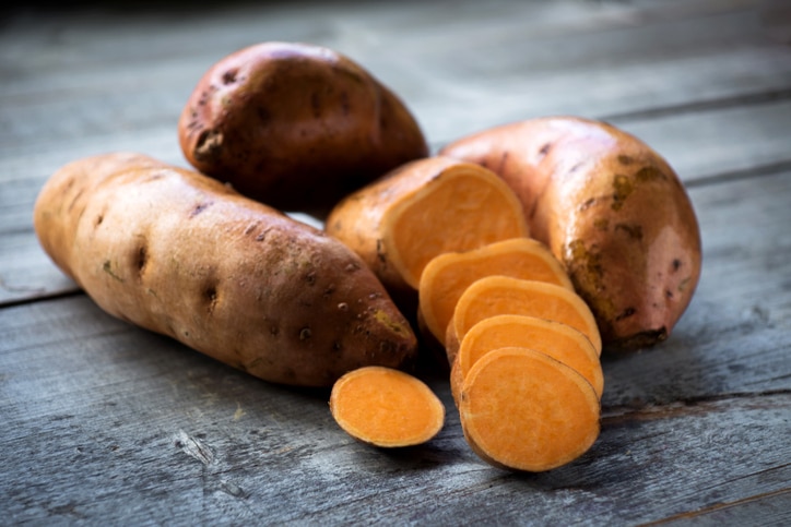 Raw sweet potatoes on wooden background closeup