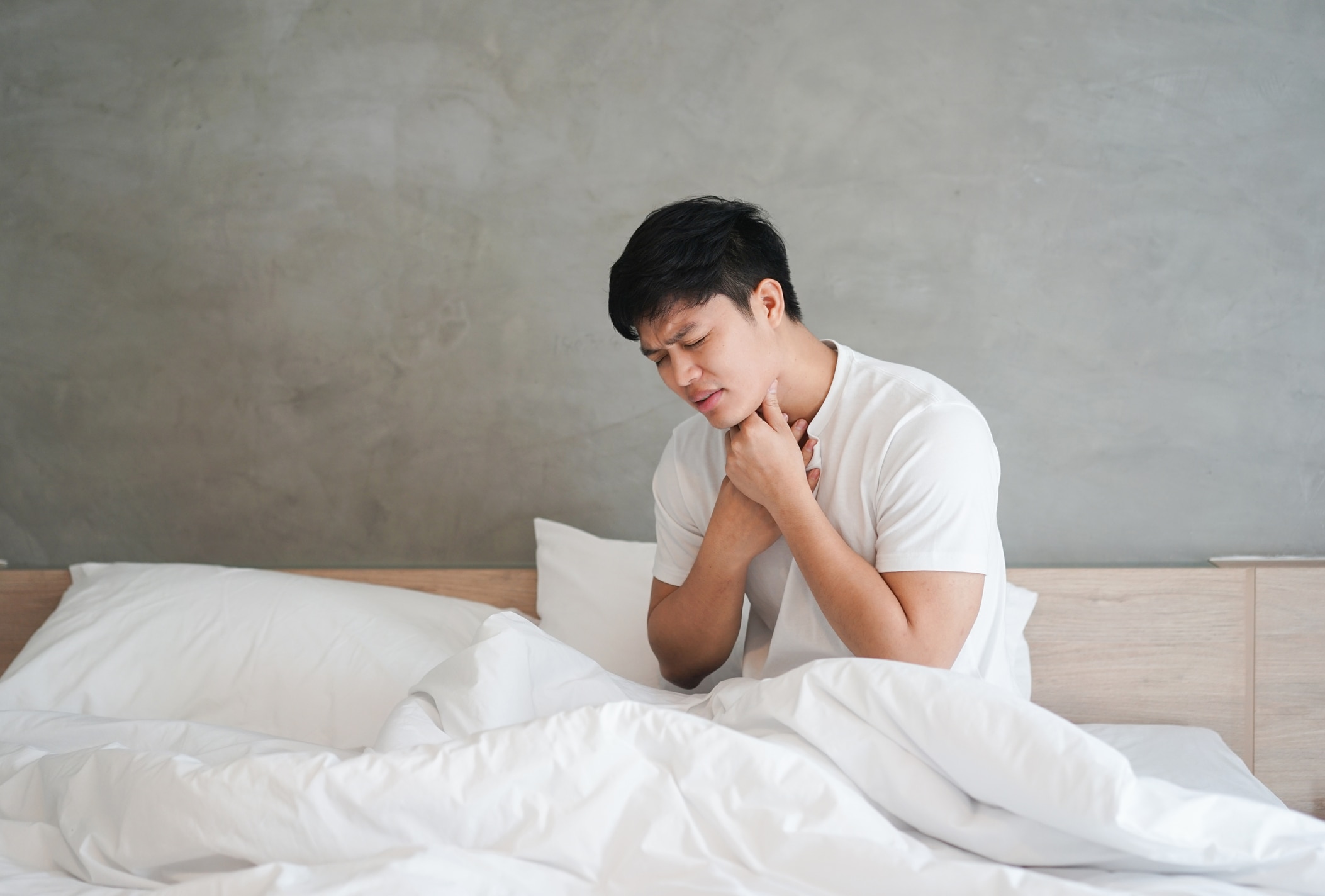 close up young asian man using hand for touching neck with feeling sore throat after wake up in the morning at bedroom , health care lifestyle people concept