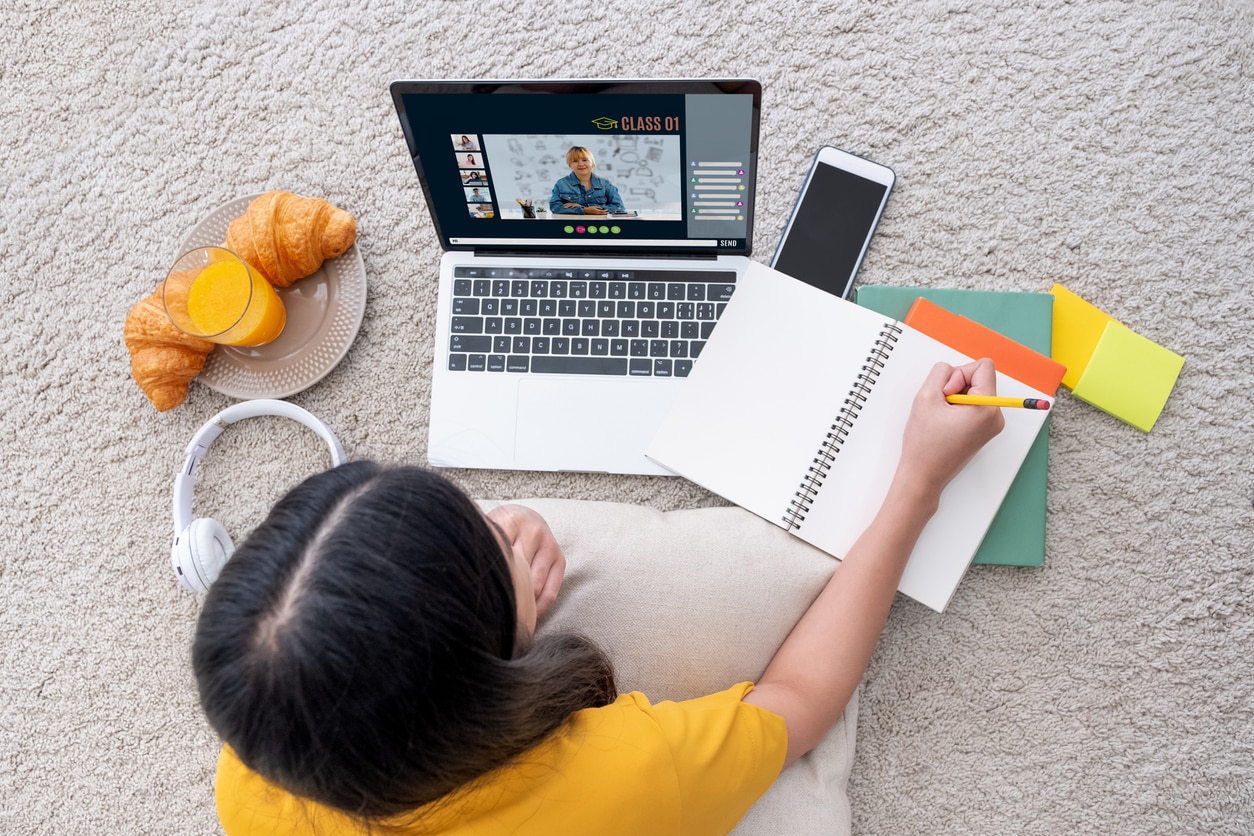 Asian female student video conference with teacher and friends using e-learing app on laptop computer at home.woman lying down on carpet.new normal learning online lifestyle