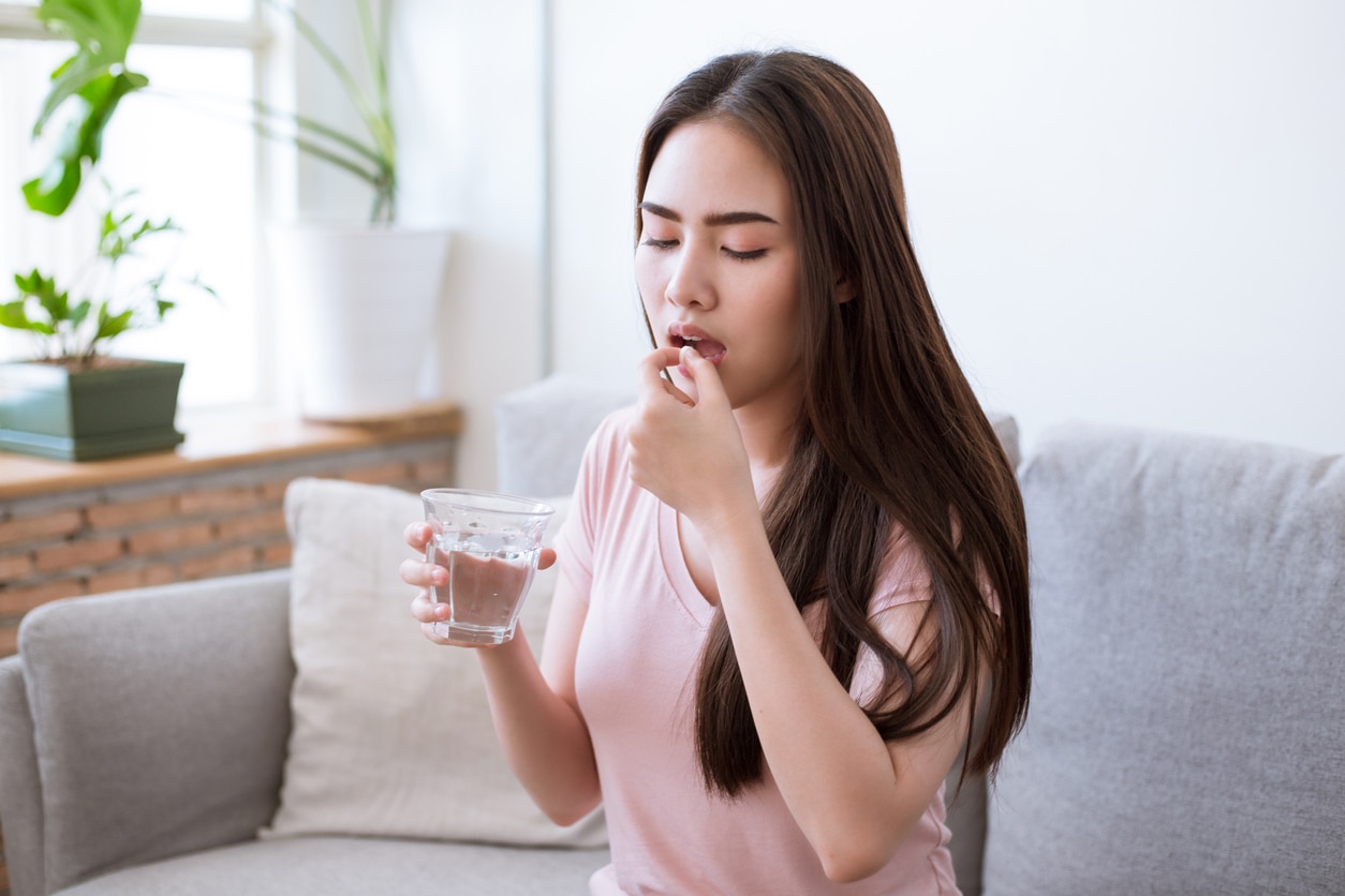 urinary tract infections can be treated with a short course of antibiotics. Sick young woman taking pills while sitting on the sofa at home