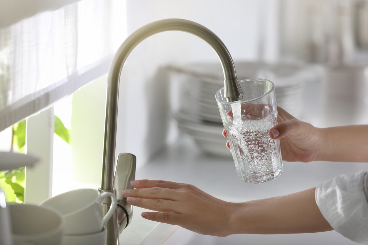 Many cities or countries will add fluoride to the drinking water to reduce tooth decay for their citizens. Woman pouring water into glass in kitchen, closeup