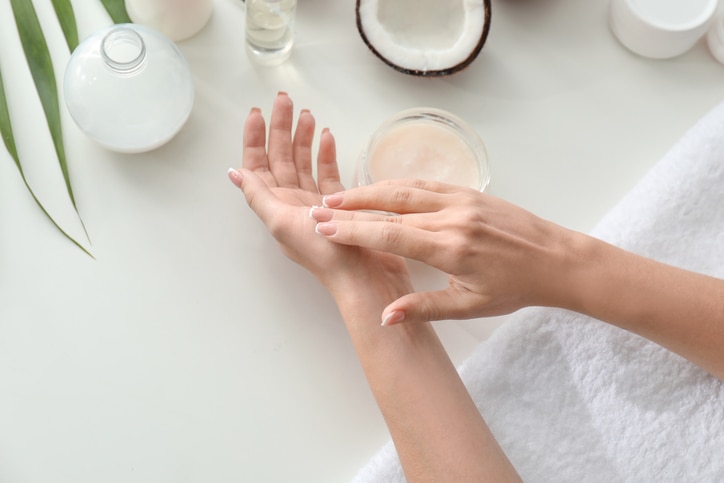 Woman applying coconut oil onto skin at white table